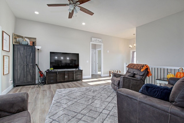 living room with ceiling fan with notable chandelier and light hardwood / wood-style flooring