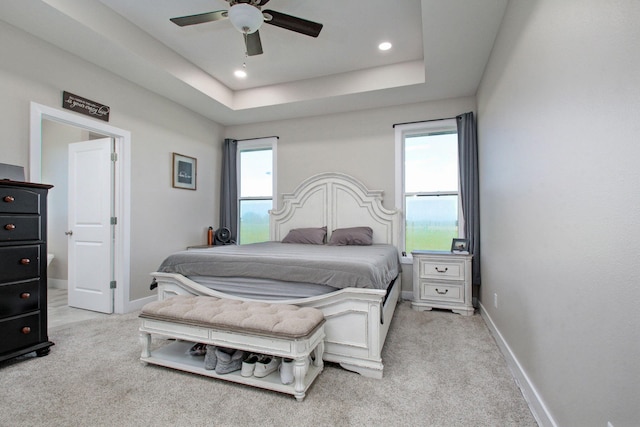 carpeted bedroom featuring a tray ceiling, multiple windows, and ceiling fan