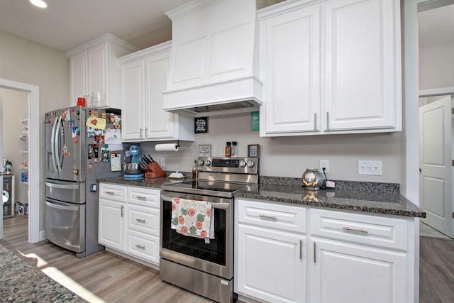 kitchen with white cabinets, custom exhaust hood, light hardwood / wood-style flooring, appliances with stainless steel finishes, and dark stone countertops