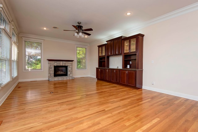 unfurnished living room featuring ceiling fan, a stone fireplace, light hardwood / wood-style flooring, and ornamental molding