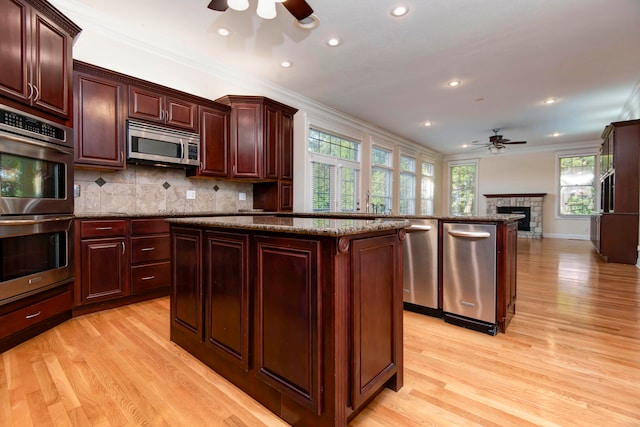 kitchen featuring light wood-type flooring, crown molding, a tile fireplace, and stainless steel appliances