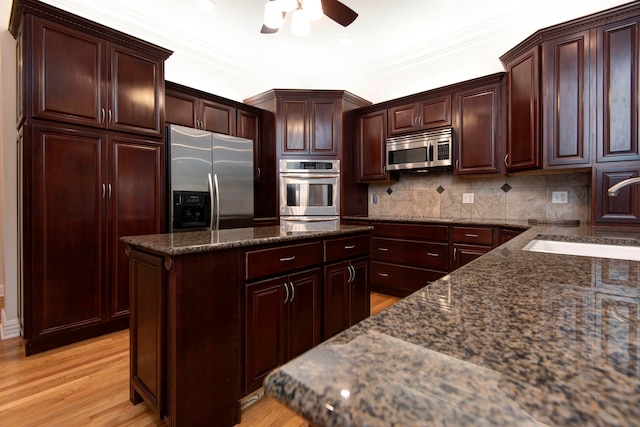 kitchen featuring light wood-type flooring, stainless steel appliances, sink, dark stone counters, and crown molding