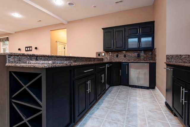 kitchen featuring light tile patterned flooring, dark stone countertops, decorative backsplash, kitchen peninsula, and dishwasher