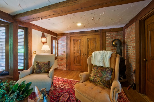 living area featuring brick wall, hardwood / wood-style floors, beam ceiling, and a wood stove