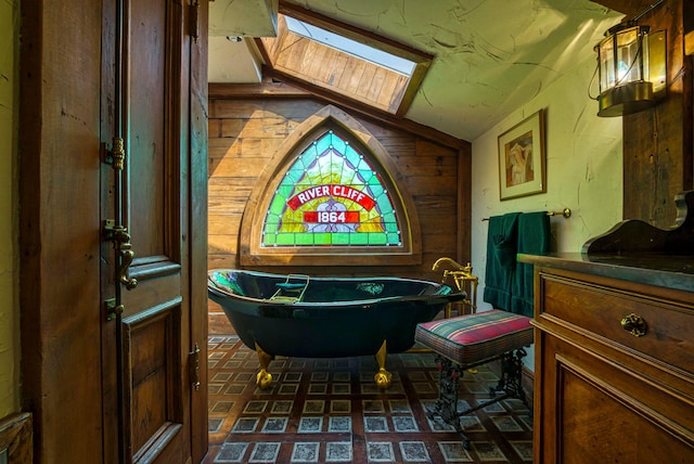 bathroom with vanity, wooden walls, vaulted ceiling with skylight, and a washtub