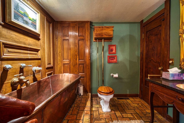 bathroom with a textured ceiling, a tub to relax in, vanity, and toilet