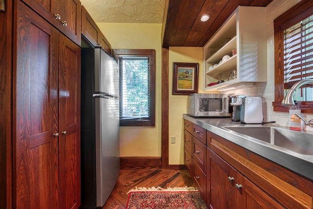 kitchen with sink, a textured ceiling, stainless steel counters, stainless steel appliances, and dark hardwood / wood-style floors