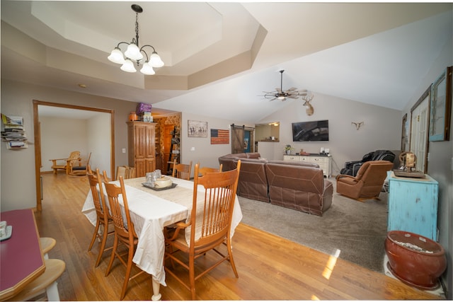 dining space featuring ceiling fan with notable chandelier, light hardwood / wood-style floors, lofted ceiling, and a raised ceiling