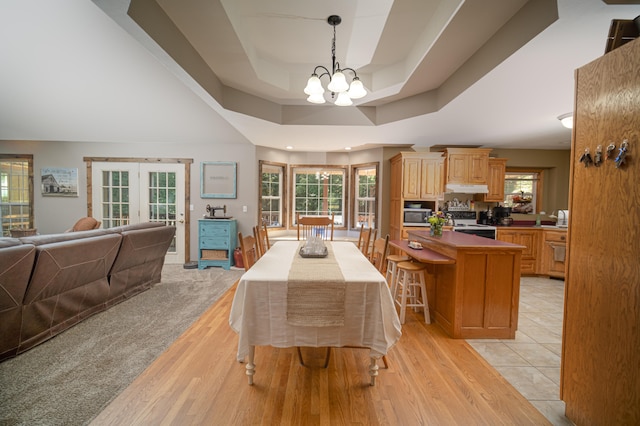 kitchen with an inviting chandelier, light wood-type flooring, a tray ceiling, a kitchen island, and hanging light fixtures