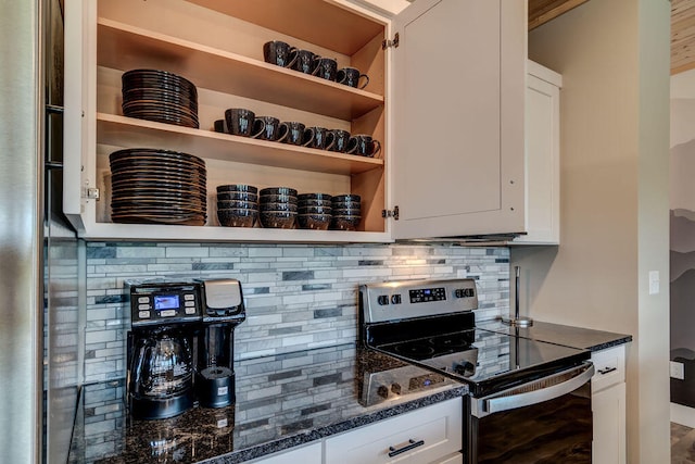 kitchen featuring dark stone counters, stainless steel range with electric stovetop, backsplash, and white cabinets