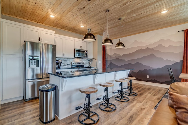 kitchen with hanging light fixtures, white cabinetry, stainless steel appliances, dark stone countertops, and light wood-type flooring