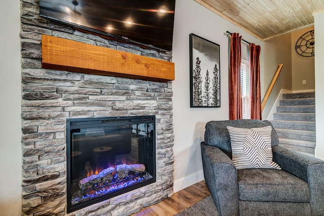 living area featuring ornamental molding, wood ceiling, hardwood / wood-style floors, and a stone fireplace