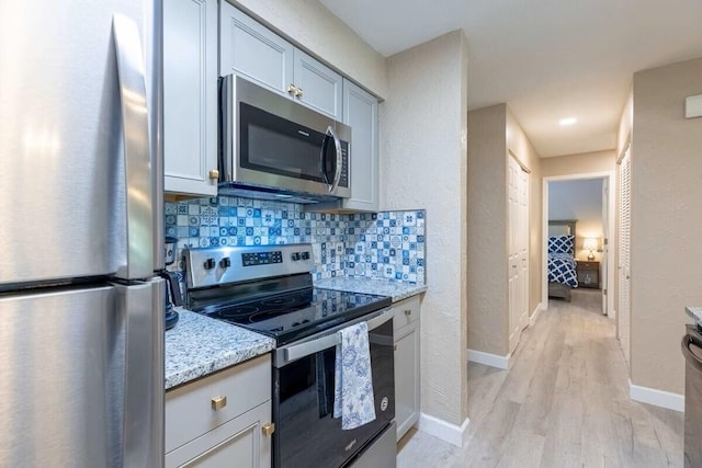 kitchen featuring light wood-type flooring, light stone countertops, stainless steel appliances, tasteful backsplash, and gray cabinetry