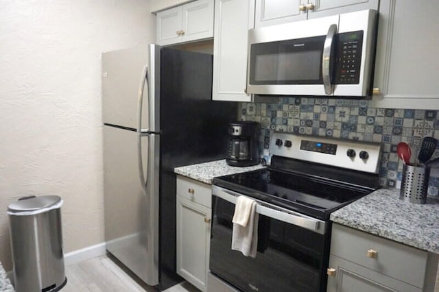 kitchen with gray cabinetry, light stone counters, decorative backsplash, and stainless steel appliances