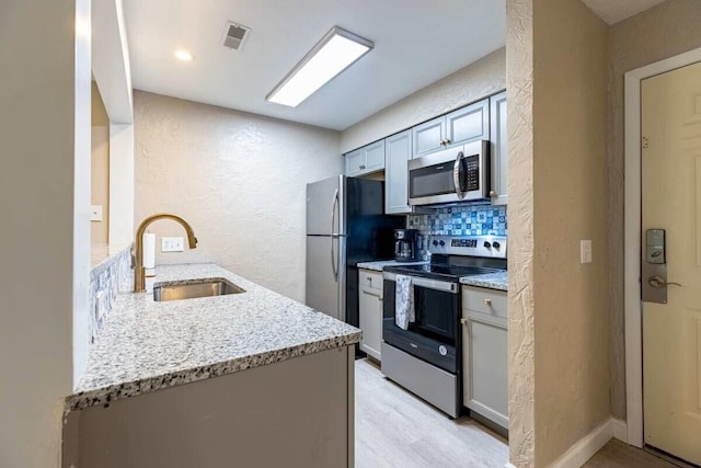 kitchen featuring light stone countertops, stainless steel appliances, sink, kitchen peninsula, and backsplash