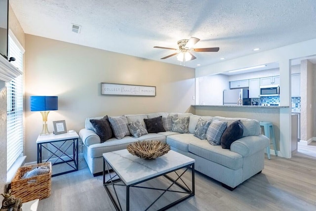 living room featuring ceiling fan, light hardwood / wood-style floors, and a textured ceiling