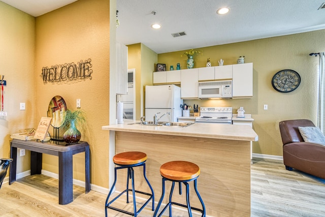 kitchen featuring white cabinets, light wood-style flooring, a sink, white appliances, and a breakfast bar area
