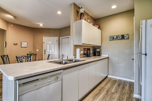 kitchen featuring dishwasher, a sink, a peninsula, light wood-style flooring, and white cabinetry