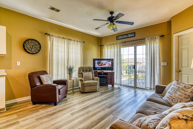 living room with light hardwood / wood-style flooring, a textured ceiling, and ceiling fan