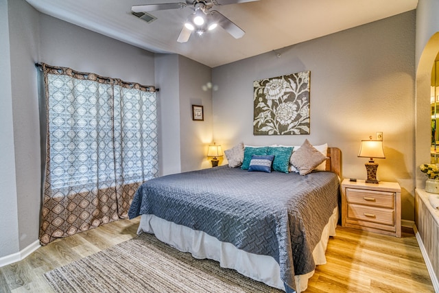 bedroom featuring light wood-type flooring, ceiling fan, arched walkways, baseboards, and visible vents