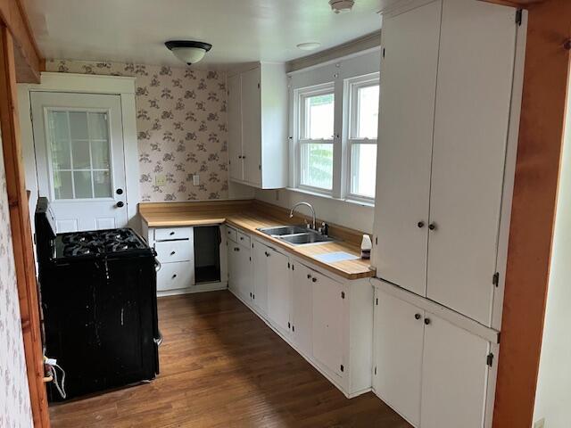 kitchen featuring black range oven, sink, dark hardwood / wood-style flooring, and white cabinetry