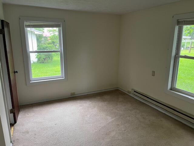 empty room with light colored carpet, a baseboard radiator, and plenty of natural light