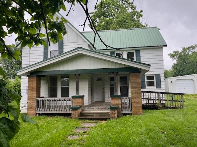 view of front of house featuring a front lawn, covered porch, a garage, and an outdoor structure