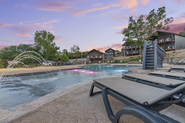 pool at dusk with a patio and pool water feature