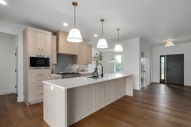 kitchen with decorative light fixtures, stove, built in microwave, an island with sink, and light brown cabinetry