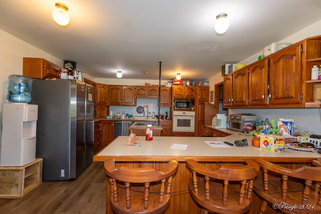 kitchen with a kitchen breakfast bar, stainless steel appliances, kitchen peninsula, and dark hardwood / wood-style flooring