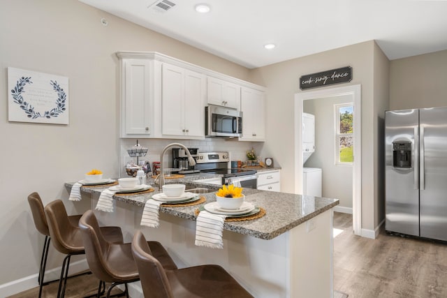 kitchen with light wood-type flooring, light stone counters, white cabinets, appliances with stainless steel finishes, and stacked washer / drying machine