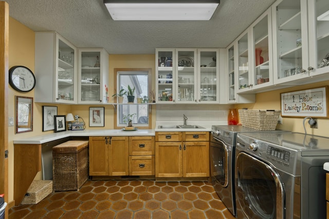 laundry area with a textured ceiling, sink, washing machine and clothes dryer, and cabinets