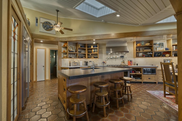 kitchen with wall chimney exhaust hood, decorative backsplash, sink, a kitchen island with sink, and stainless steel microwave