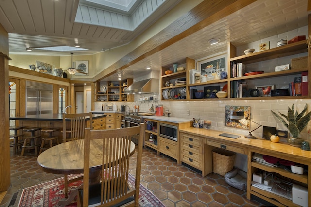 kitchen featuring vaulted ceiling, wall chimney range hood, decorative backsplash, sink, and built in appliances