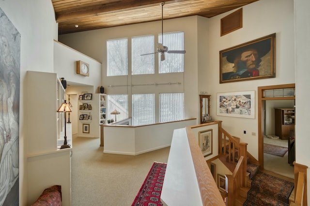 interior space featuring wood ceiling, ceiling fan, carpet floors, a high ceiling, and beamed ceiling