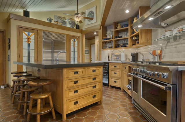 kitchen with lofted ceiling, backsplash, extractor fan, a center island with sink, and high end appliances