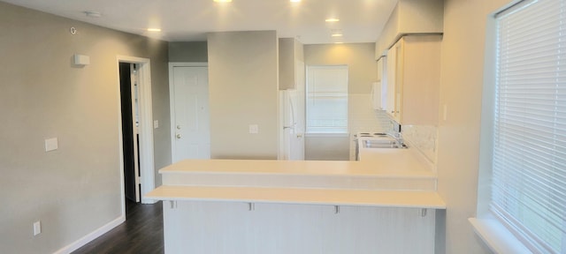 kitchen featuring kitchen peninsula, backsplash, dark wood-type flooring, white cabinetry, and a breakfast bar