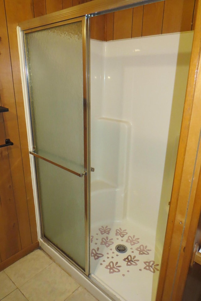 bathroom with tile patterned flooring, a shower with door, and wood walls