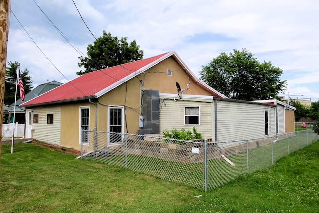 rear view of house with metal roof, a lawn, stucco siding, and fence