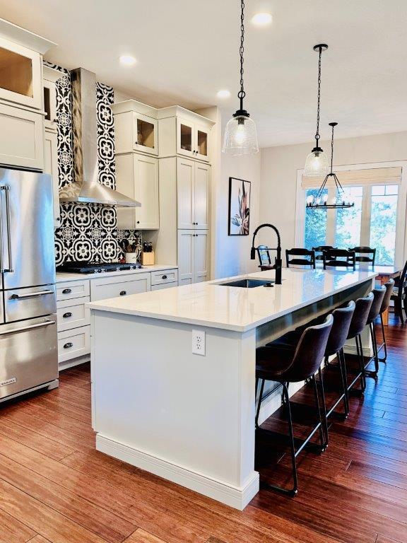 kitchen with high quality fridge, dark hardwood / wood-style floors, wall chimney range hood, a center island with sink, and a kitchen breakfast bar