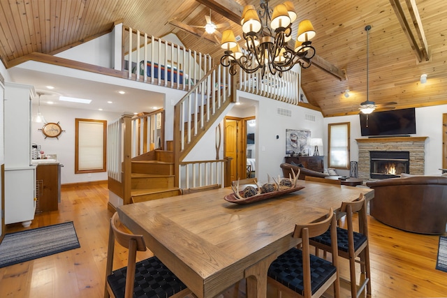 dining space featuring light hardwood / wood-style floors, wooden ceiling, beam ceiling, a fireplace, and high vaulted ceiling