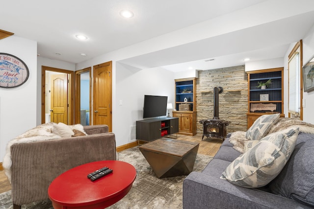 living room featuring built in features, light hardwood / wood-style flooring, and a wood stove