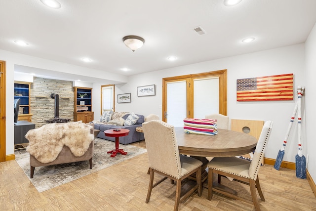 dining room featuring a wood stove, built in shelves, and light hardwood / wood-style floors