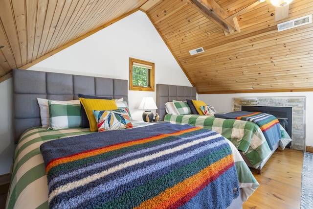 bedroom with lofted ceiling with beams, hardwood / wood-style flooring, a stone fireplace, and wood ceiling