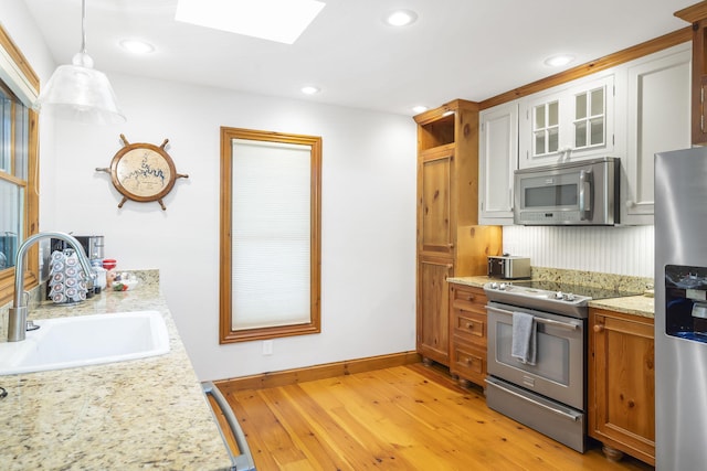 kitchen featuring light hardwood / wood-style flooring, decorative light fixtures, sink, white cabinets, and appliances with stainless steel finishes