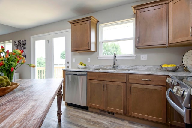 kitchen featuring appliances with stainless steel finishes, sink, light stone counters, and light hardwood / wood-style flooring