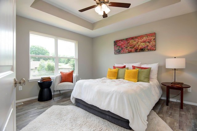 bedroom with hardwood / wood-style floors, ceiling fan, and a raised ceiling