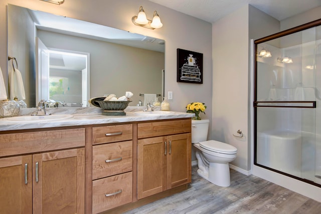 bathroom with hardwood / wood-style flooring, a shower with shower door, vanity, and toilet