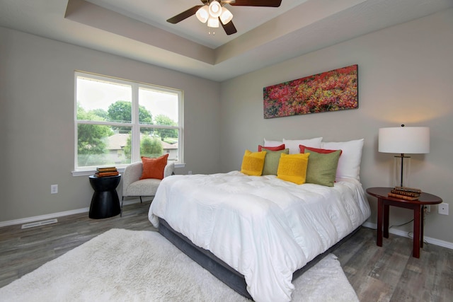 bedroom with dark hardwood / wood-style flooring, ceiling fan, and a tray ceiling