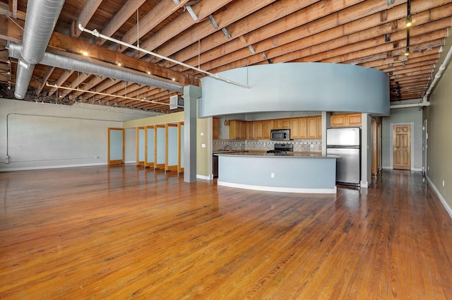 interior space featuring backsplash, appliances with stainless steel finishes, and hardwood / wood-style flooring